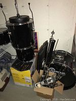 Disassembled black Gammon Pro drum kit including bass drum, toms stacked on box, and hardware in cardboard box