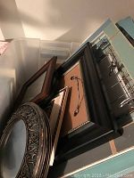 Photo of assorted picture frames including blue painted frame with wire and clips and several wood frames stacked together