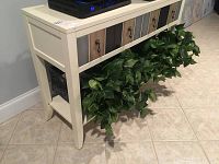 Front side view of the white side table with multi-toned drawers, woven baskets underneath, and green faux plants flowing from the shelf.