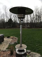 Full view of the propane patio heater standing on outdoor stone patio with grass background.