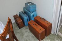 Photo showing the two sets of luggage stacked on carpet, 3 tan Samsonite suitcases and 3 blue American Tourister suitcases.