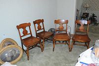 Four of the six maple dining room chairs arranged side by side showing the wood finish, shape of the backrest and legs.