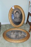Two vintage oval gold decorative picture frames side by side on floor showing front with black and white portraits. Frames are about 25x19 inches.