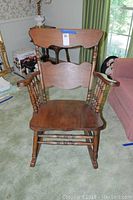 Front view of vintage wooden rocking chair showing the seat, armrests, and backrest with two horizontal wooden panels and spindles.