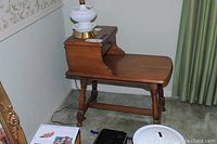 Side view of a maple vintage side table with a drawer, showing turned legs and stepped top design, with a lamp placed on it.