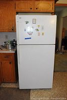 Front view of white top freezer Kenmore refrigerator with magnets and notes on door.