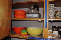 Shelf with two stacked orange Anchor Hocking casserole dishes and three nested colorful Pyrex bowls below.