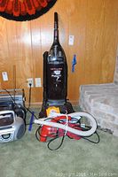 Hoover Wind Tunnel Ultra self-propelled upright vacuum with Dirt Devil handheld vacuum and accessories on the floor beside it.