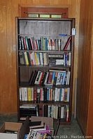 Front view of wooden 5-shelf bookcase filled with assorted books on each shelf.
