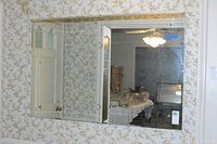 Rectangular wall mirror with beveled edges mounted on floral wallpapered wall, reflecting white door and dining table setup.