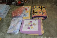 Three handmade quilts and three blankets folded and placed on carpet for display.