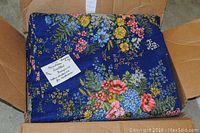 Folded navy floral quilted bedspread with a note stating it is new and includes extra curtain fabric.