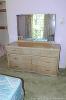Full front view of the wooden 7-drawer dresser with attached beveled mirror reflecting window/curtains.