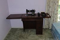 Front view of the White Rotary sewing machine mounted on the wooden cabinet with foldable tables extended, showing the sewing machine, cabinet top, and drawers.
