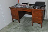 Wooden desk with medium brown finish, six drawers closed, wires and office equipment on the top