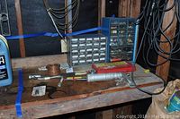Overview of garage workbench with organizer drawers filled with small hardware items, caulking gun, coils of wire, and various small tools scattered on wooden surface.