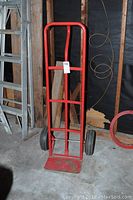 Front view of the red metal furniture dolly showing the handle, frame, platform, and wheels.
