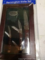 Photo of the three folding knives with wooden handles and brass bolsters inside the wooden case with the Remington Knife Set packaging.