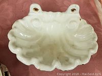 Top view of white cast enameled soap dish showing shell shape and mounting holes with wear.