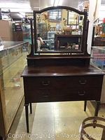 Front view of dark wood vanity style dresser with attached mirror and two drawers.