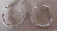 Photo showing pair of sterling silver twisted rope hoop earrings on a flat surface. Earrings approximately one inch in size with twisted rope design and sterling backs.