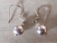 Pair of sterling silver ball pierced earrings on a light fabric background, showing both earrings side by side.