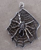 Front view of sterling silver spider web pendant with spider and black stone body on beige fabric background.