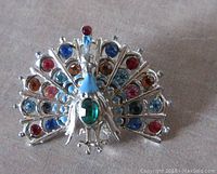 Front view of vintage silver tone peacock brooch adorned with red, blue, green, orange, and aquamarine rhinestones, with blue enameled neck detail.