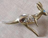 Front view of a metal kangaroo brooch featuring clear rhinestones on the shoulder and a single blue glass rhinestone eye.
