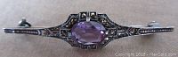 Top frontal view of the Art Deco sterling silver brooch showing the oval facetted amethyst center and marcasite accents.