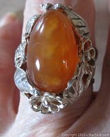 Close-up front view showing large polished teardrop-shaped carnelian stone set within an intricate open flower and leaf sterling silver design.
