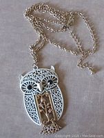 Full view of articulated owl pendant on gold tone chain showing front design details with pierced and floral motifs.