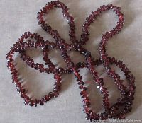 Full view of garnet chip necklace arranged in a loose loop on a neutral surface, showing the deep red stone chips and length.