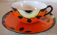 Oblique side view of vintage cup and matching saucer with bright orange black floral design.
