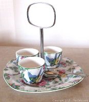 Set of three floral chintz patterned egg cups with bluebird design placed on matching oval serving tray with metal handle and a small silver spoon, showing detailed floral and bird artwork and condition.