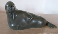 Full side view of the seal soapstone carving on a flat surface, showing shape and details including the raised flipper and tail.