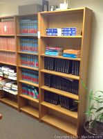 Photo of two light wood finish bookshelf units holding many books, primarily law reference books and binders. Located in an office setting.
