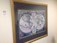 Framed antique-style world map hung on wall, showing details of the dual hemispheres and decorative border.
