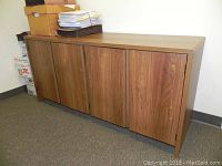 Front view of wood-finish office storage unit with four cabinet doors, showing scratches and wear.