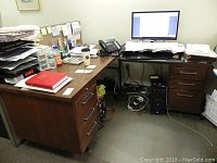 Photo of L shaped office desk with computer and paperwork on top, showing overall item condition and layout in office.