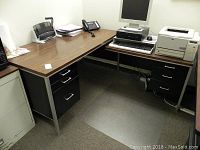 L-shaped office desk with woodgrain laminate surface, black metal drawer units with silver handles, and metal legs.