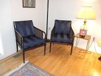 Two caned chairs side by side with blue striped cushions and dark walnut finish, placed on hardwood floor next to small table and lamps.