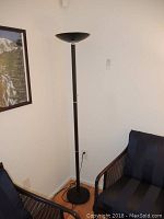 Full view of black torchiere floor lamp standing beside wall and furniture, showing base and assembled stand.