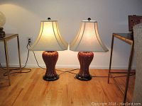 Wide view of both lamps side by side on a wooden floor with fabric shades and electrical cords visible.