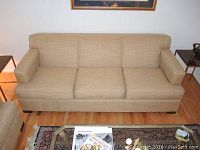 Front view of tan fabric couch showing three seat cushions and armrests