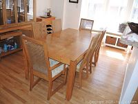 Dining table with six chairs set in a room with wood flooring and furniture. Shows table surface marks.