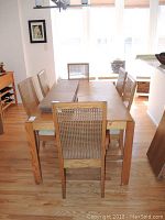 Six teak Bernhardt dining chairs arranged around a dining table, showing wood tone and cane backs.