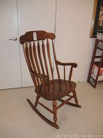 Front angle showing the full wooden rocking chair with spindle back and curved armrests in a room.