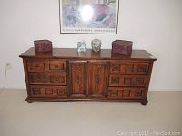 Front view of a wooden dresser showing multiple drawers and central cabinet doors with decorative carving. The surface has some decorative items placed on top.