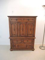 Front view of wooden chest of drawers showing three upper panel doors, four drawers, and metal handles
